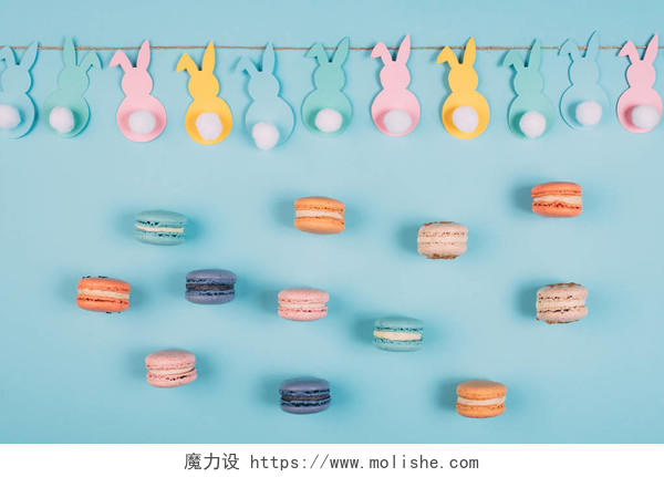 复活节兔子花环和蓝色表面彩色马卡龙的顶级视图